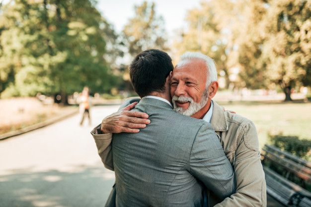 elderly man hugging younger man in suit joyfully outdoors in park