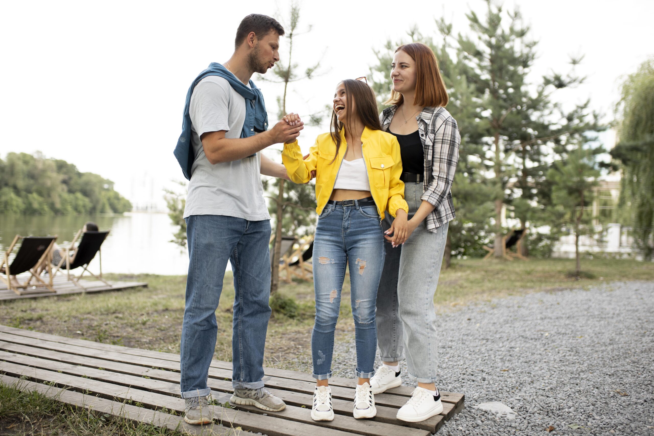 two women and one man laughing and talking together outdoors near lake